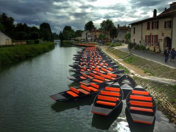 Boats moored in canal at city against cloudy sky