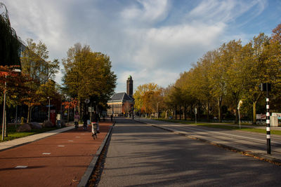 Road amidst trees and buildings in city against sky