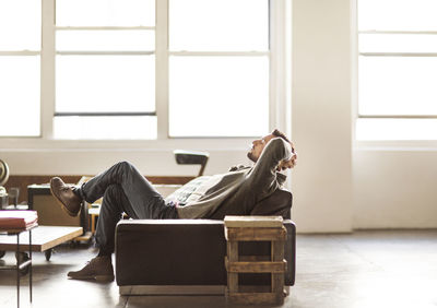 Side view of businessman relaxing on sofa in brightly lit creative office