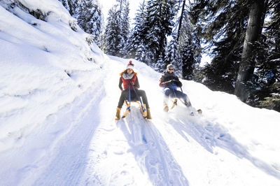 Couple sledding on snow during sunny day in winter