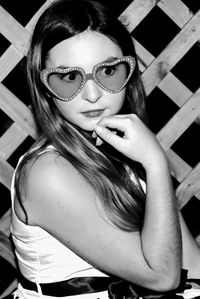 Woman wearing novelty glasses standing with hand on chin against fence