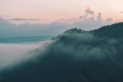 Scenic view of fog covered mountains against sky during sunset