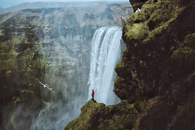 Man standing on rock by waterfall