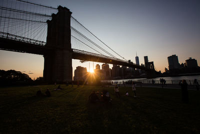 People on suspension bridge over river against sky during sunset