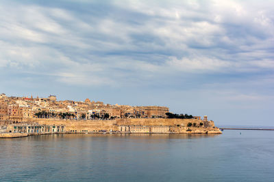 View of buildings by sea against cloudy sky