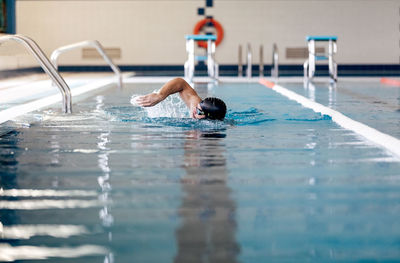 Male swimmer in cap and goggles performing sidestroke while swimming in rippled pool