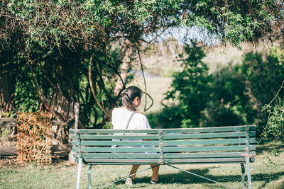 Rear view of woman sitting on bench in park