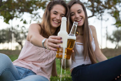 Happy friends enjoying beer while sitting on grass at park