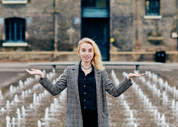 Portrait of young woman gesturing while standing against fountain