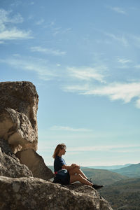 Woman sitting on rock looking at mountain against sky