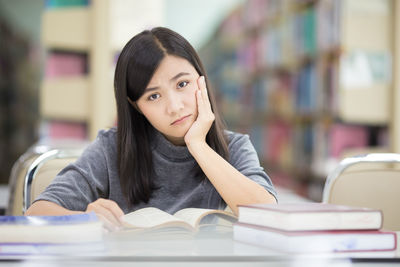 Young woman reading book while sitting at table in library