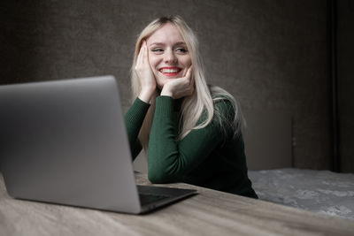 Happy smiling blonde girl in green golf joyfully works online at home with a laptop. 
