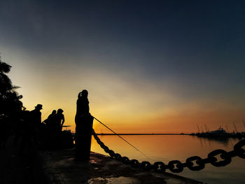 Silhouette people standing on beach against sky during sunset