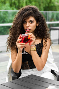 Portrait of young woman holding a drink while sitting outdoors