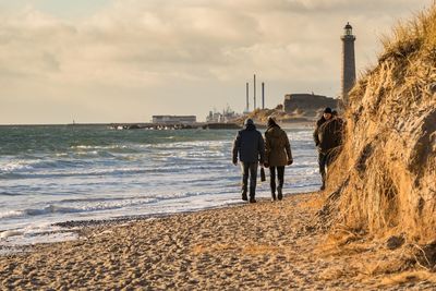 Rear view of men walking on beach against sky