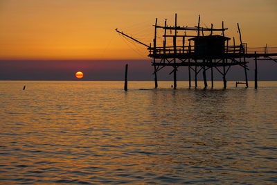 Silhouette built structure over sea against sky during sunset