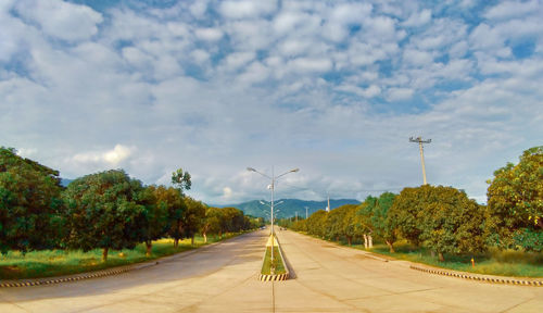 Empty road amidst trees against sky