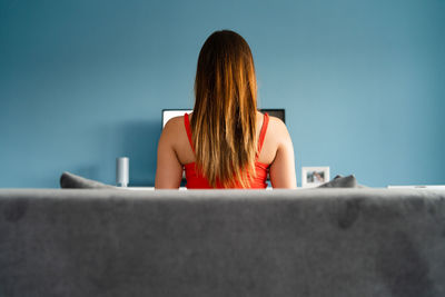 Rear view of woman watching tv while sitting on sofa at home