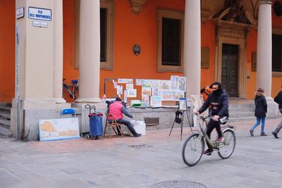 People riding bicycle on street against building