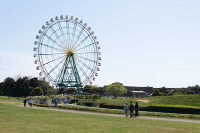 People by ferris wheel on field against sky