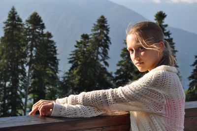 Portrait of young woman leaning on railing against trees