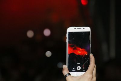 Cropped hand of woman photographing illuminated red stage at night