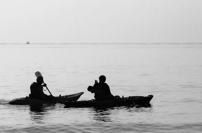 Men kayaking in sea against clear sky