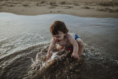 Baby boy playing in water at beach during sunset