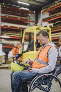 Male carpenter with disability using digital tablet sitting on wheelchair in warehouse