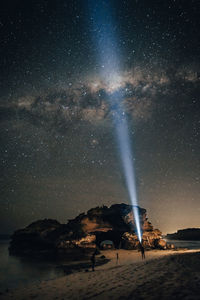 Man pointing flashlight towards stars in sky