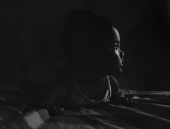 Close-up of baby girl looking away while lying on bed in darkroom at home