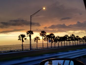 Road by trees against sky during sunset