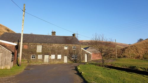 Road by buildings against clear blue sky