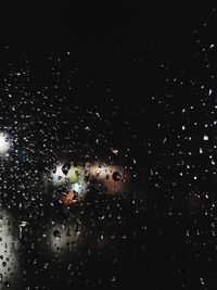 Close-up of wet glass window against black background
