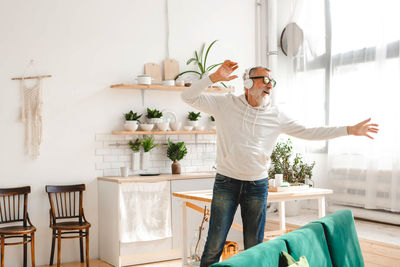 Full length of woman with arms raised standing at home