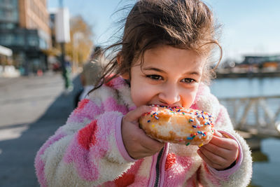 Young girl eating donut with sprinkles outside