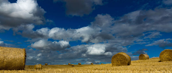 Hay bales on agricultural field against sky