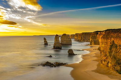 Scenic view of sea with rock formations at beach against sky during sunset