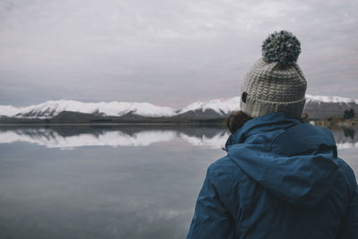 Young woman on a blue jacket stares at lake tekapo, southern alps