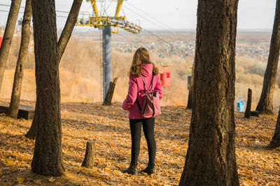 Rear view of woman standing by tree trunk