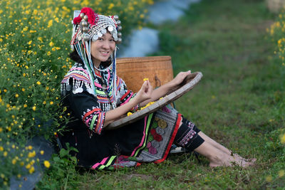 Woman holding umbrella while sitting on field