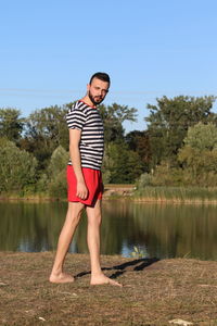 Full length of man standing by lake against clear sky