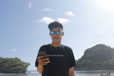 Portrait of young man standing on mobile phone against sky