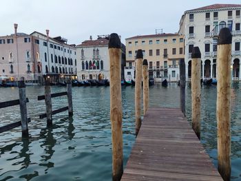 Wooden posts in canal amidst buildings against sky