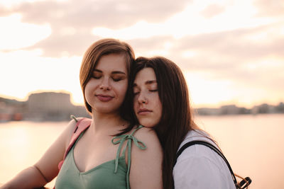 Portrait of happy lesbian couple standing on bridge at sunset