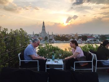 Rear view of man and woman sitting against buildings at sunset