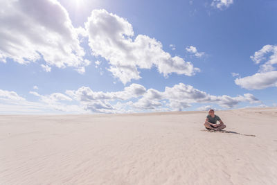 Man sitting on sand dune in desert against sky