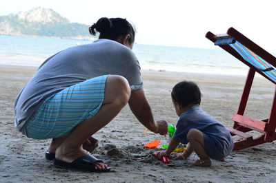 Side view of mother and daughter playing with toys while crouching at beach