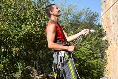 Side view of young man holding rope against trees