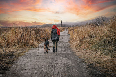 Rear view of people walking on road against sky during sunset